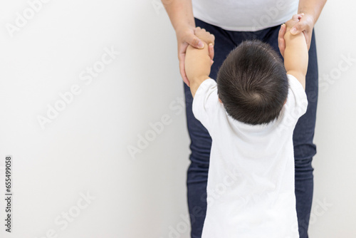 母親と手をつないでつかまり立ちする赤ちゃんの後ろ姿（男の子、生後9カ月、1歳、日本人）
