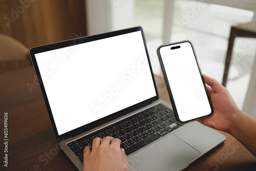 mockup image computer,cell phone blank screen for hand typing text,using laptop contact business searching information in workplace on desk at office.design creative work space on wooden desk