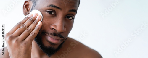 Man care. Face hygiene. Confident satisfied shirtless guy cleansing cheeks facial skin with tonic on cotton pad isolated on white background empty space.