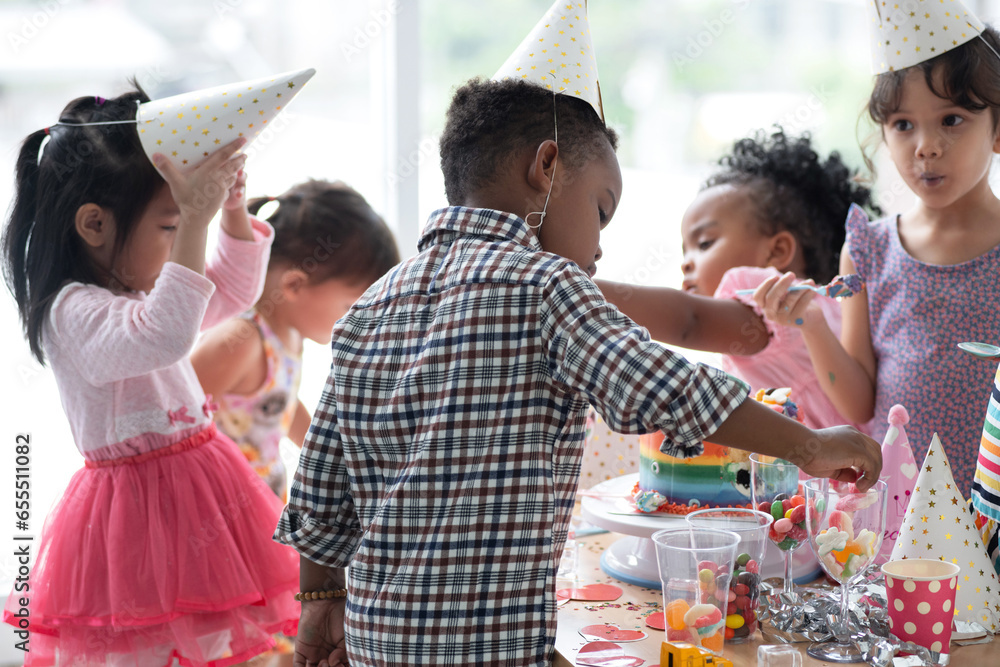Obraz premium Group of multiracial little boy and girls enjoy eating beautiful rainbow cakes and candy in party