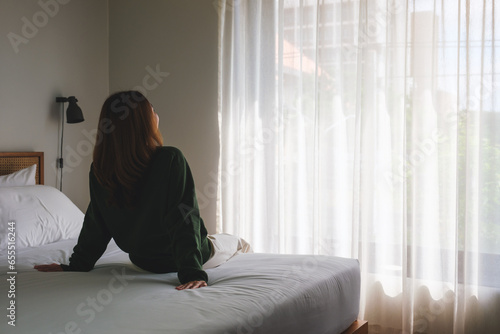 Rear view image of a woman sitting relaxing on a bed after waking up in bedroom