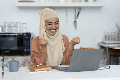 Surprised and happy businesswoman raises her arms to express joy after viewing and knowing business approval and financial approval results on laptop at home office. startup business growth ideas