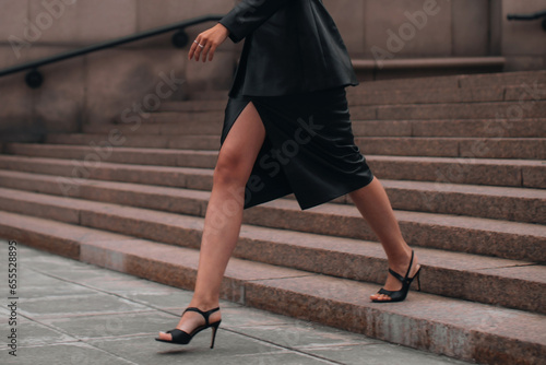 Fashionable details of a black leather skirt, jacket and high heels. Woman walking in the city. Street style cloth concept