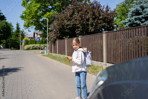 Child looks at a cell phone while crossing a road in front of the car. Concept of mobile phone addiction.