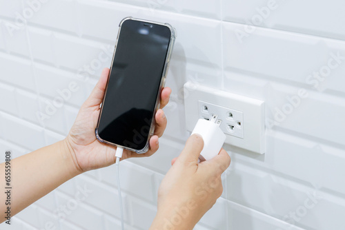 Hand holding smart phone and adaptor to connect to power outlet wall, Hand pluging adapter with outlet socket plug and hold mobile.
