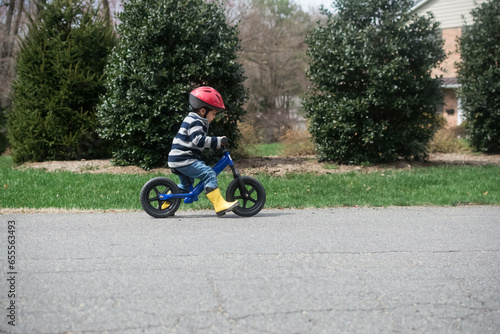 Young boy riding balance bike on suburban street.