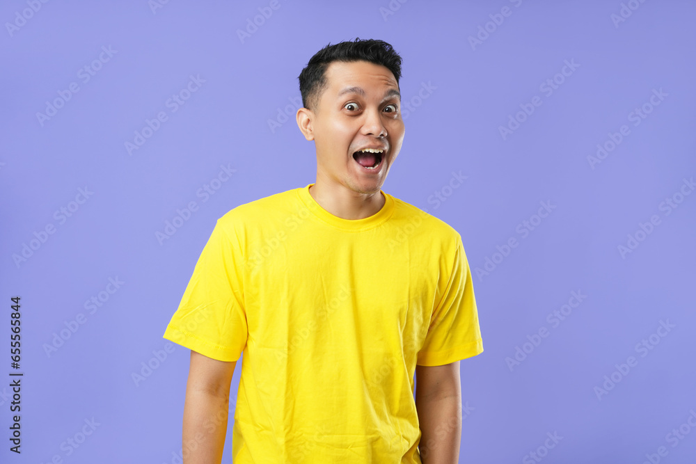Medium photo of posing Asian man with big eyes and wide-open mouth. Wearing a yellow t-shirt, isolated on a soft blue background. Medium photo of posing Asian man with big eyes and wide-open mouth. Wearing a yellow t-shirt, isolated on a soft blue background.