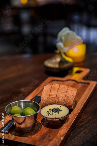 Slices of sourdough bread, butter with black salt and green olives on a wooden board at a fine dining restaurant in Seattle, Washington, USA