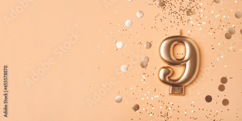 Gold candle in the form of number nine on peach background with confetti.