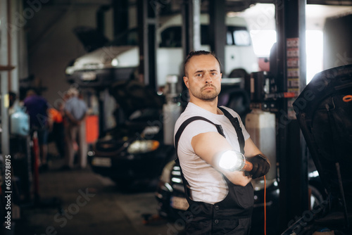 Portrait of a young beautiful car mechanic in a car workshop, in the background of service. Concept: repair of machines, fault diagnosis, repair specialist, technical maintenance and on-board computer