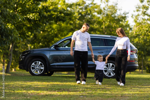 Car is behind. Happy family is in the park at summer time together.