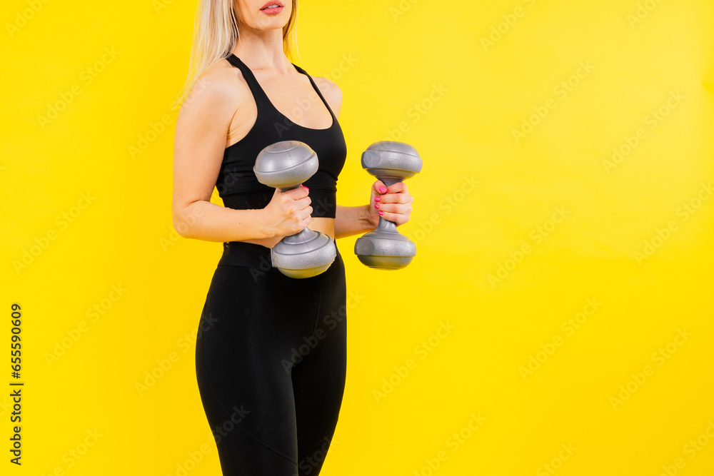 Fototapeta premium Sporty woman does the exercises with dumbbells on dark, yellow, red background.
