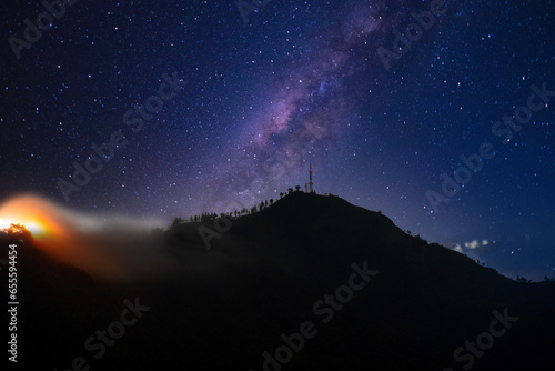 Communication mobile phone tower on peak of mountain standing out with clouds fog rolling over hills with lights of city in distance
