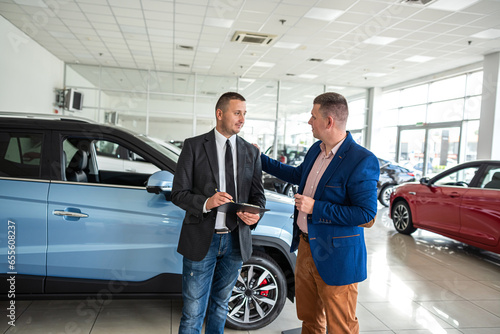 Customer buying a modern car with help a professional male manager at car dealership