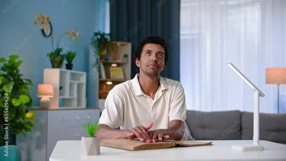 young black man with poor eyesight reads a book and runs his fingers along page while studying text while sitting at a table at home young black man with poor eyesight reads a book and runs his fingers along page while studying text while sitting at a table at home
