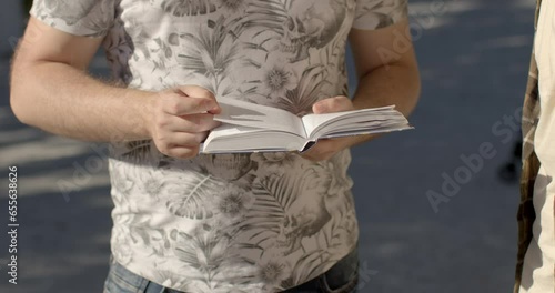 Close-up book in the hands of a young man. Students discuss the text with Deep interest in the subject matter, sharing insights, debating viewpoints, expressing their fascination with the narrative.