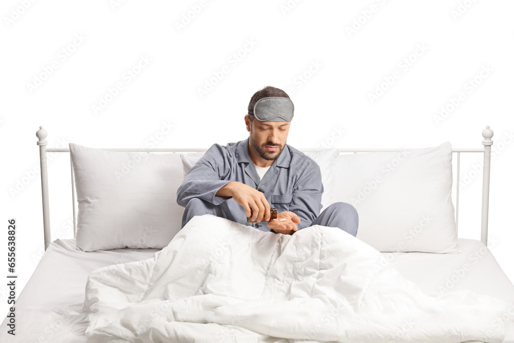 Man in pajamas sitting in a bed and holding a bottle of pills Man in pajamas sitting in a bed and holding a bottle of pills