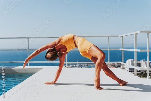 Beautiful young atlethic woman wearing sportswear doing yoga meditation on the terrace rooftop with sea view - Yoga practicer training outdoors, healthy lifestyle, sport and meditation concepts