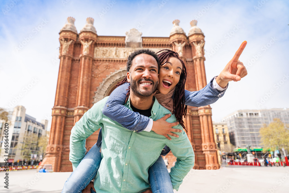 Beautiful happy hispanic latino couple of lovers dating outdoors - Tourists in Barcelona having fun during summer vacation and visiting Arc de Triumf historic landmark - obrazy, fototapety, plakaty 