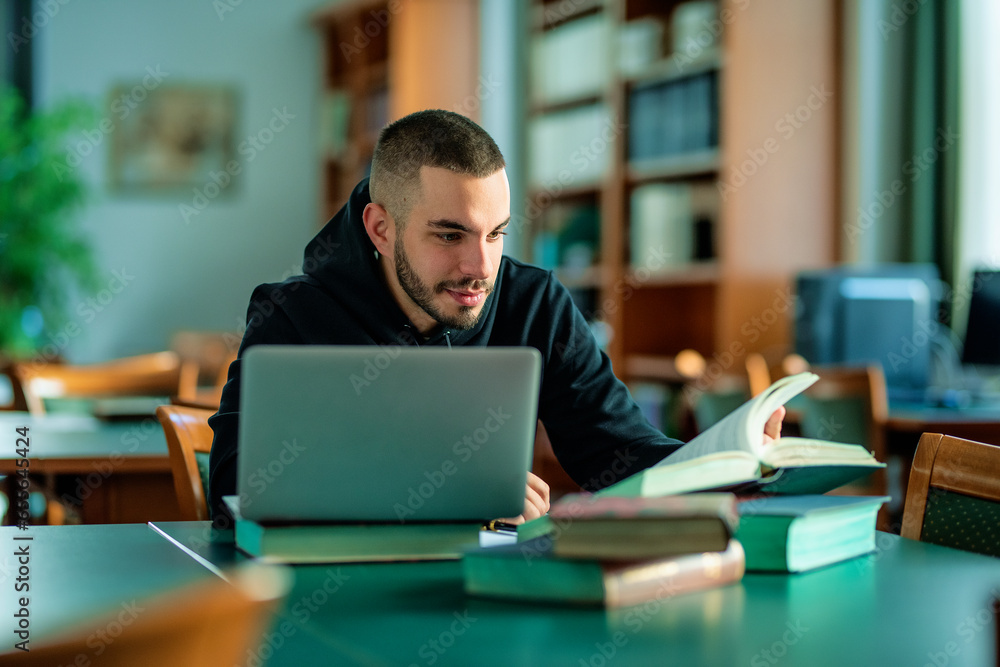 Male student using notebook and books and learning in the university library Male student using notebook and books and learning in the university library