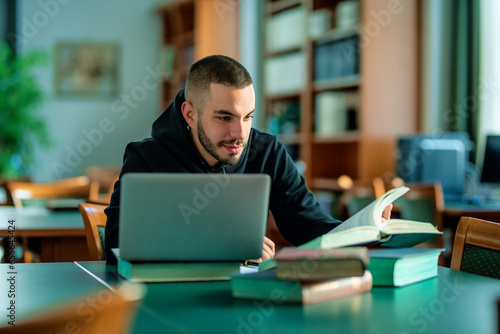 Male student using notebook and books and learning in the university library