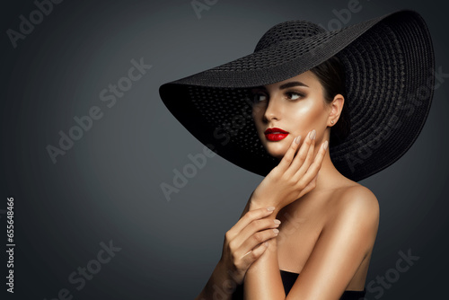 Fashion Woman in Black Wide brim Hat with Red Lips Makeup side view. Elegant Lady Portrait looking away over Gray. Beautiful Model Make up and Hands Manicure showing Earring