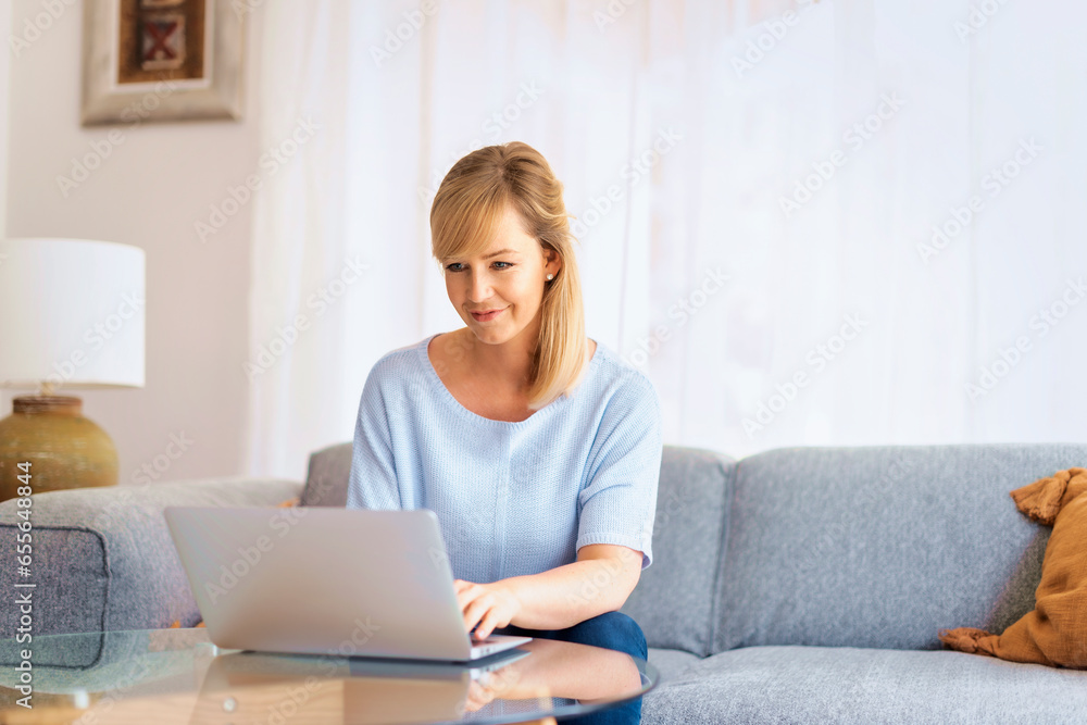 Blond haired woman sitting at home and using laptop for work Blond haired woman sitting at home and using laptop for work
