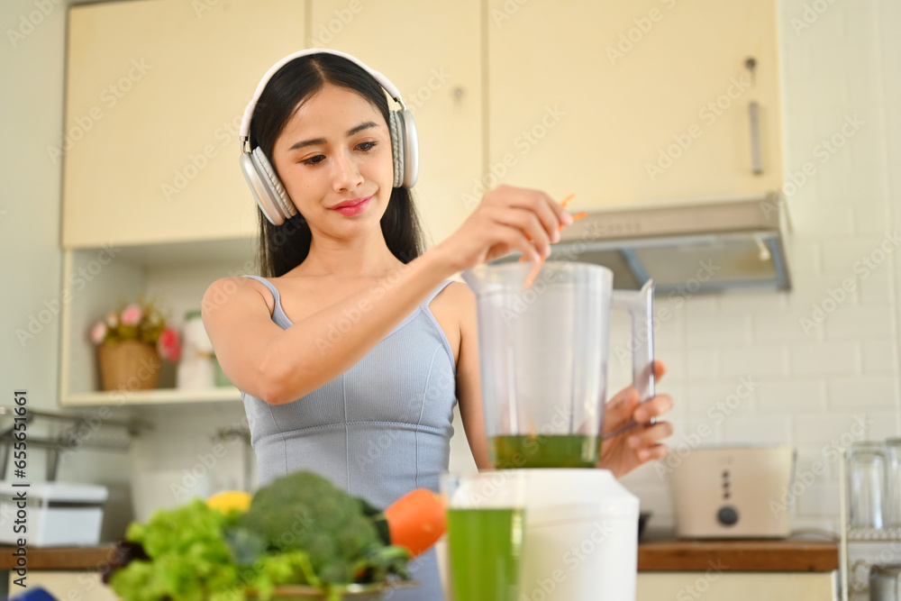 Young woman in headphone making healthy smoothie for weight loss and detox in kitchen. Healthy lifestyle concept