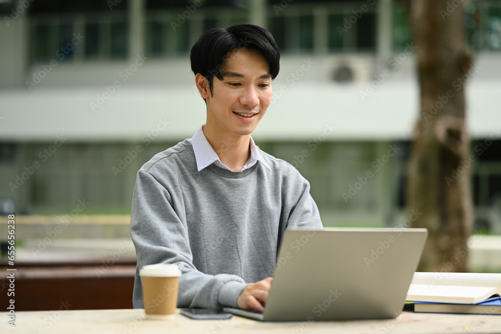 Handsome man using laptop, preparing for exam on table at campus. Youth lifestyle and education concept Handsome man using laptop, preparing for exam on table at campus. Youth lifestyle and education concept