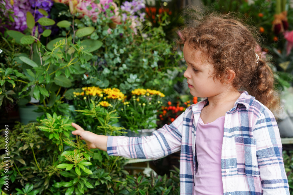 Cheerful cute child girl with curly hair looking plants in the flower shop Cheerful cute child girl with curly hair looking plants in the flower shop