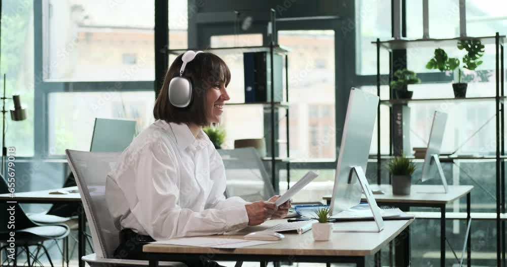 A cheerful office worker, holding documents, conducts a video call within the office. Her friendly smile and efficient multitasking are on display as she engages in a virtual meeting. A cheerful office worker, holding documents, conducts a video call within the office. Her friendly smile and efficient multitasking are on display as she engages in a virtual meeting.