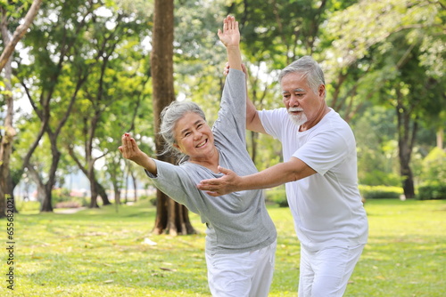 Asian senior couple practice yoga excercise, tai chi tranining, stretching and meditation together with relaxation for healthy in park outdoor after retirement. Happy elderly outdoor lifestyle concept