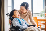 Portrait of beautiful asian mother playing and smiling with her young son on wheelchair, cherishing quality time together, child with disabilities