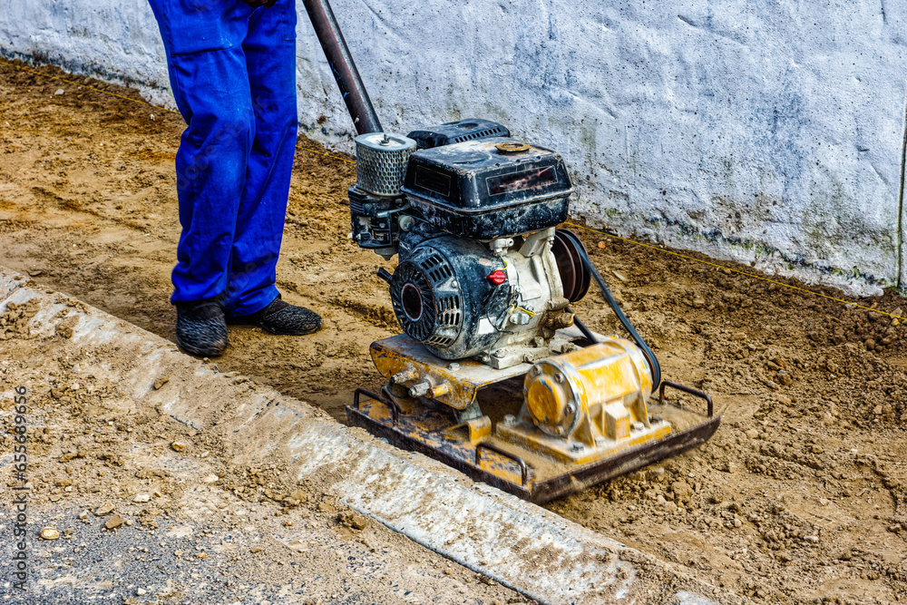 Worker using gas-powered compactor to compact sand on verge before paving