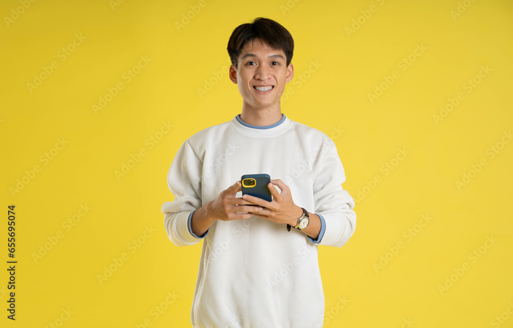 portrait of young Asian man wearing sweater and using phone on yellow background portrait of young Asian man wearing sweater and using phone on yellow background