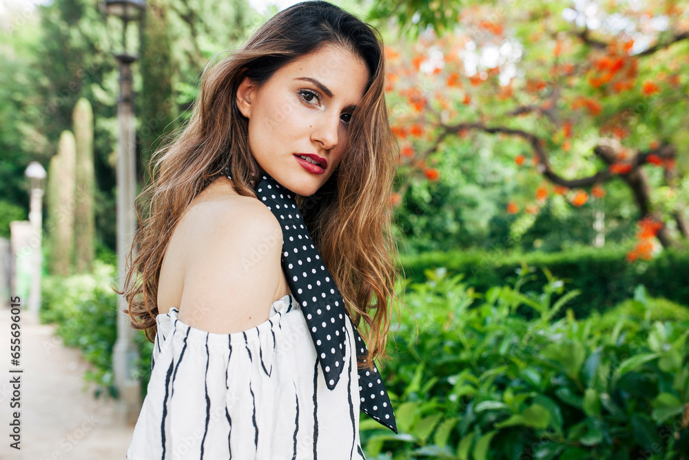 Relaxed young attractive elegant woman standing in park with a white dress and black scarf, looking at camera. Relaxed young attractive elegant woman standing in park with a white dress and black scarf, looking at camera.