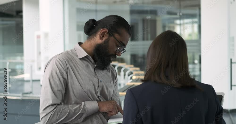 Within the office corridor, an Indian manager and a Caucasian woman manager engage in a conversation. Their discussion reflects the interplay of diverse perspectives. Within the office corridor, an Indian manager and a Caucasian woman manager engage in a conversation. Their discussion reflects the interplay of diverse perspectives.