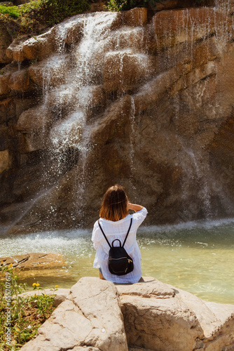 Fototapeta Naklejka Na Ścianę i Meble -  Woman sitting on a rock near a waterfall
