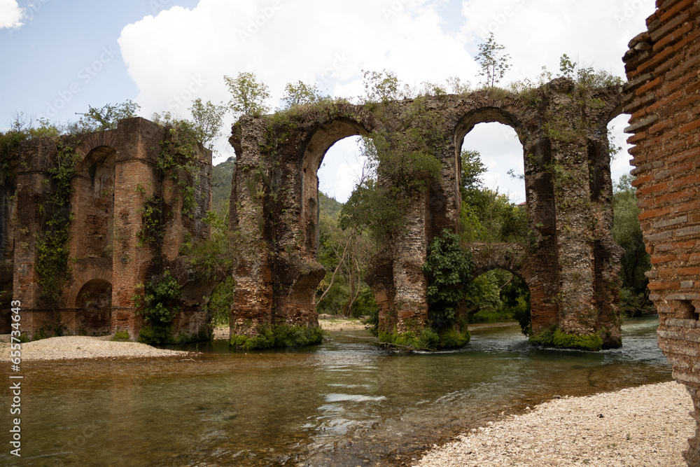 Ancient roman aqueduct with a river and plants at filipiada Greece summer natural light v7