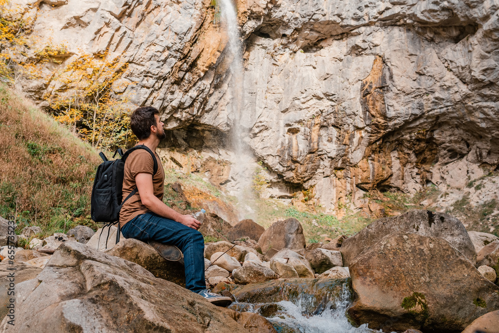 A male traveler enjoying near the mountain river waterfall.