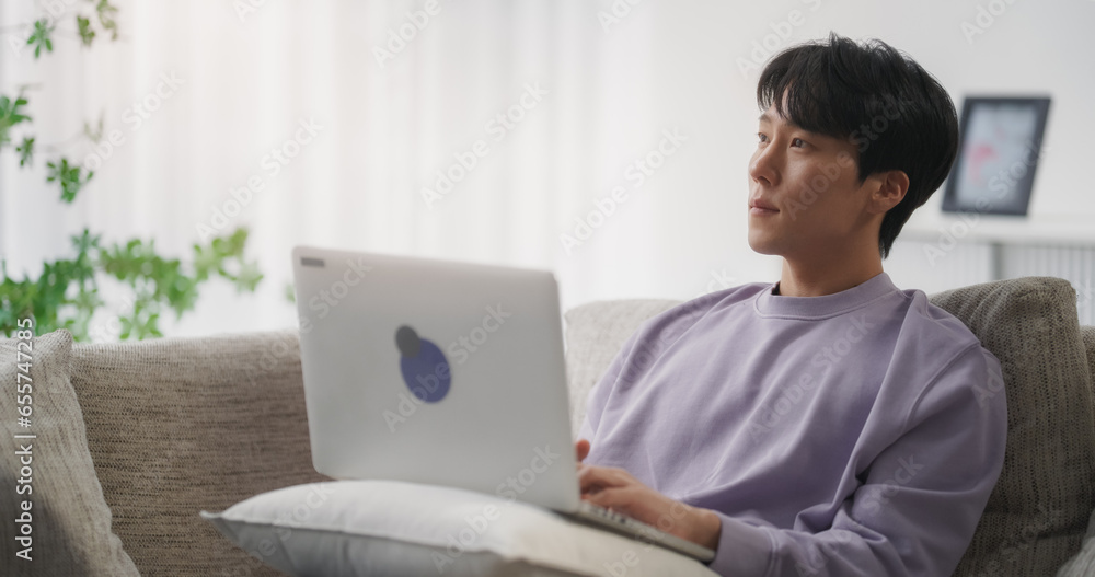 Young Handsome Asian Male Browsing Internet, Using Laptop Computer at Home, Online Shopping for Electronics on Social Media Marketplace While Sitting on a Couch in the Living Room Young Handsome Asian Male Browsing Internet, Using Laptop Computer at Home, Online Shopping for Electronics on Social Media Marketplace While Sitting on a Couch in the Living Room