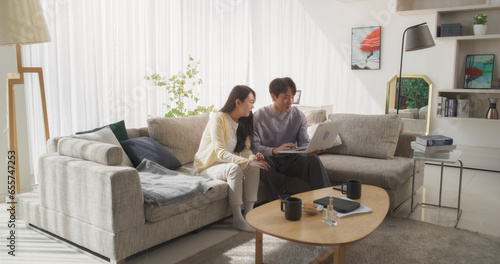 South Korean Couple Spending Casual Time Together in a Cozy Apartment, Creating Memories on the Sofa with Their Laptop Computer, Editing and Manipulating Beautiful Photographs