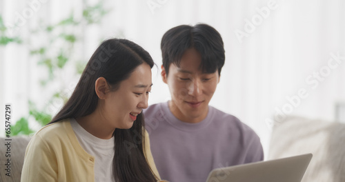 Portrait of a Happy South Korean Couple Spending Quality Time at Home, Creating a Harmonious Atmosphere in Their Cozy Apartment, Streaming and Enjoying a K-Drama TV Show on a Laptop Computer © Kitreel