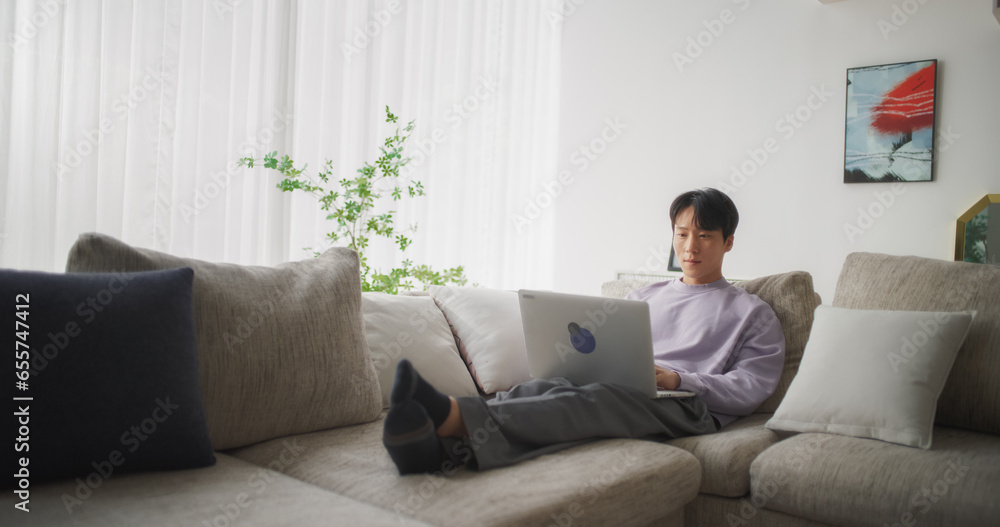 South Korean Male Working from Home, Using his Laptop Computer to Optimize Performance and Achieve Goals, Creating Engaging Content and Managing Social Media Campaigns from a Home Workspace