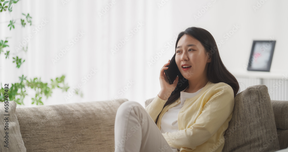 Sitting on the Sofa in Her Cozy Apartment, Beautiful Smiling South Korean Woman is Having a Thoughtful Phone Conversation, Sharing Happy Stories of Love and Friendship with Genuine Emotion Sitting on the Sofa in Her Cozy Apartment, Beautiful Smiling South Korean Woman is Having a Thoughtful Phone Conversation, Sharing Happy Stories of Love and Friendship with Genuine Emotion