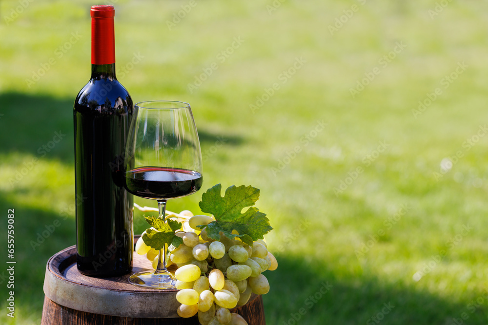 Fototapeta premium Wine bottle, red win glass and grape on barrel