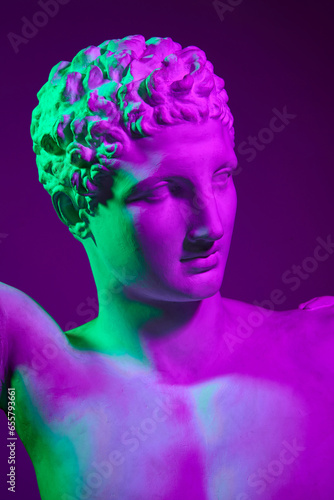Gypsum statue of man, antique statue bust against purple studio background in neon lights. Concept of antique style, classic art, museum, history and mythology. Poster, ad