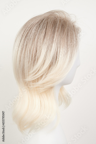 Natural looking blonde fair wig on white mannequin head. Middle length hair cut on the plastic wig holder isolated on white background  side view.