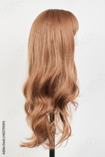 Natural looking dark blonde wig on white mannequin head. Long fair hair cut on the plastic wig holder isolated on white background