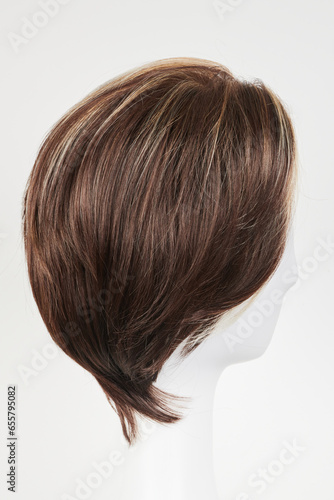 Natural looking dark brunet wig on white mannequin head. Short brown hair on the plastic wig holder isolated on white background, side view.